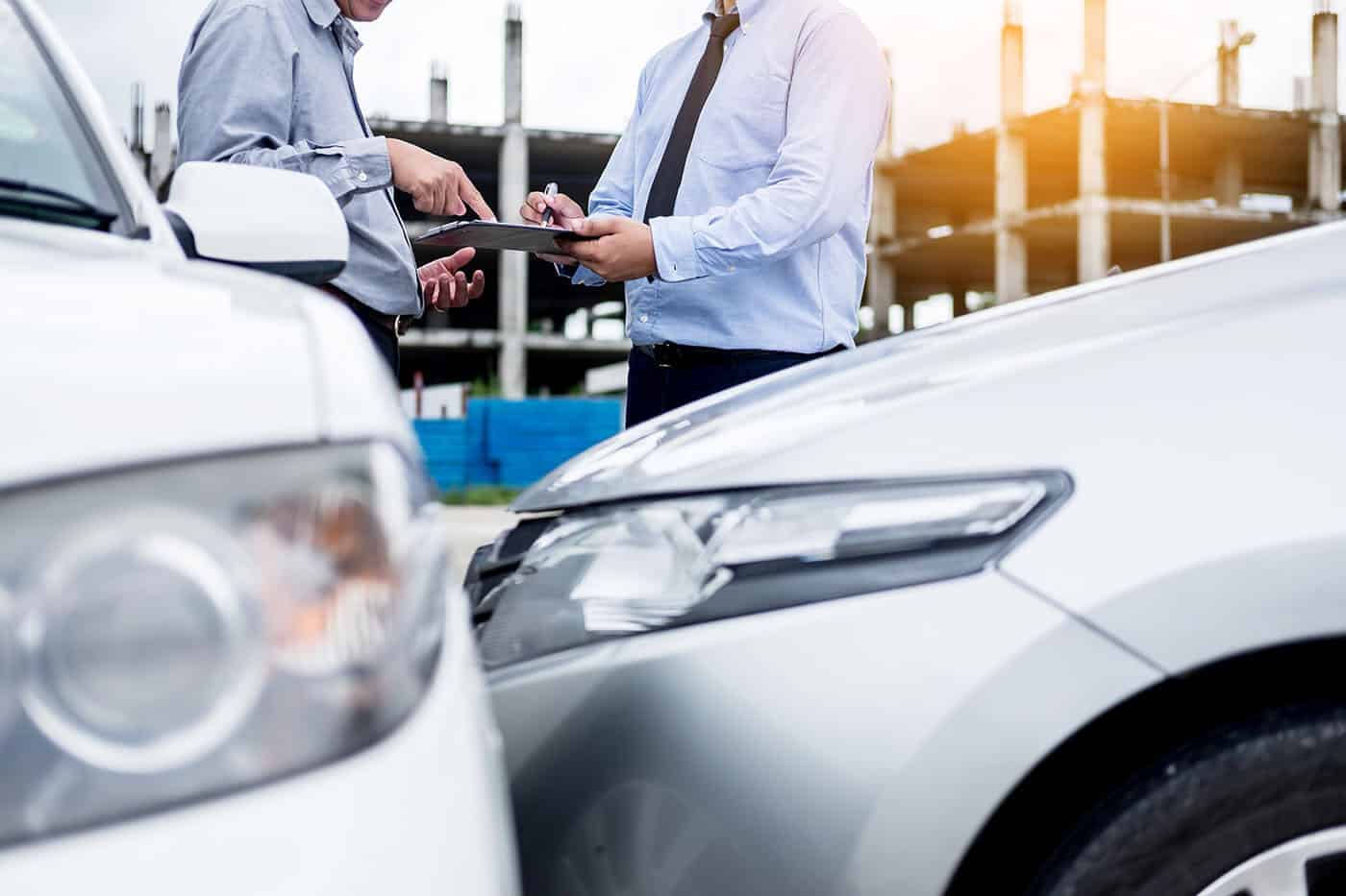 Insurance agent writing on clipboard while examining car after a